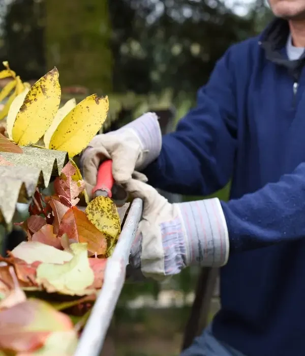 Person cleaning leaves and debris from a gutter with gloves and a tool, demonstrating professional gutter maintenance services in Monroe, NC.
