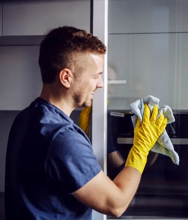 Man wearing yellow gloves cleaning a window with a microfiber cloth, showcasing professional window cleaning services relevant to APS Charlotte in Indian Trail, NC.
